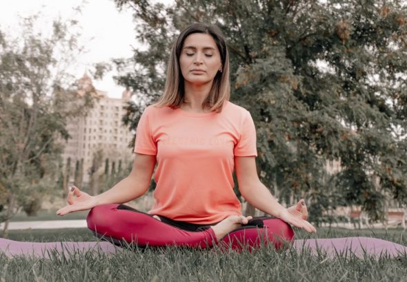 Adult woman practicing meditation on a yoga mat outdoors in a tranquil park setting.