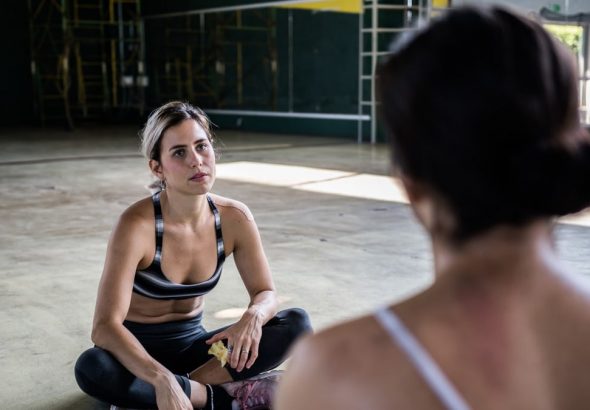 Two women in a workout session, sitting on the gym floor, focused and relaxed.
