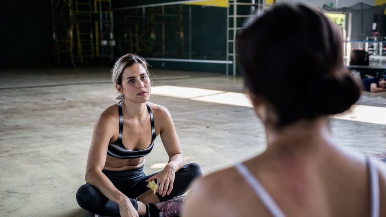 Two women in a workout session, sitting on the gym floor, focused and relaxed.