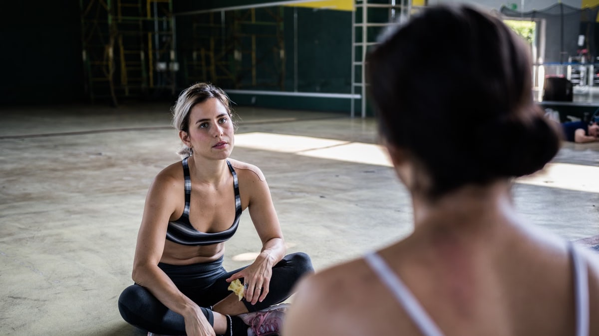 Two women in a workout session, sitting on the gym floor, focused and relaxed.